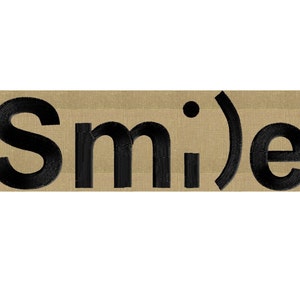 Może przedstawiać: Beige naszywka z czarnym haftem z napisem "Smile".