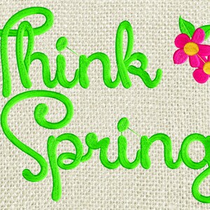 May include: Green embroidered text on a beige fabric background reads "Think Spring!" with two pink flowers to the right of the text.