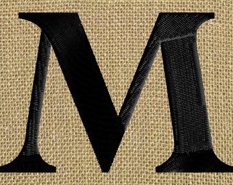 May include: Black embroidered letter M on a burlap background.
