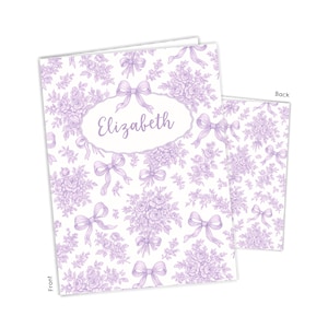 May include: A set of two notebooks with a floral and bow pattern in lavender and white. The front notebook has the name "Elizabeth" in an oval frame. The back of the notebook is visible, showing the same pattern.
