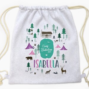 May include: White drawstring bag with a camping scene printed on it. The scene includes a cabin, trees, a lake, tents, animals, and the text "Camp Timberlane 2021" and "Isabella".