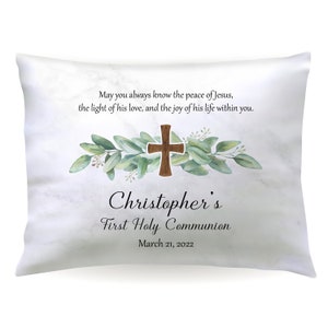 May include: White pillow with a marble pattern featuring a green leafy garland with a brown wooden cross. The text reads "May you always know the peace of Jesus, the light of his love, and the joy of his life within you. Christopher's First Holy Communion March 21, 2022"