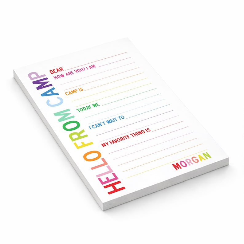 May include: A rectangular notepad with white paper featuring the vertical text HELLO FROM CAMP in rainbow colors on the left. The page includes fill-in-the-blank lines with prompts like DEAR, HOW ARE YOU, CAMP IS, TODAY WE, I CAN'T WAIT TO, and MY FAVORITE THING IS, with the name MORGAN printed at the bottom right.