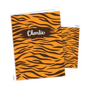 May include: A rectangular greeting card featuring an orange and black tiger stripe pattern. The front of the card displays a dark brown horizontal brushstroke shape with the name Charlie written in white script text across the center.