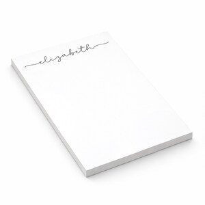 May include: A rectangular white notepad featuring the name elizabeth printed in a black cursive script font at the top. The notepad consists of a stack of paper sheets with a clean, plain surface below the text, presented at an angle.