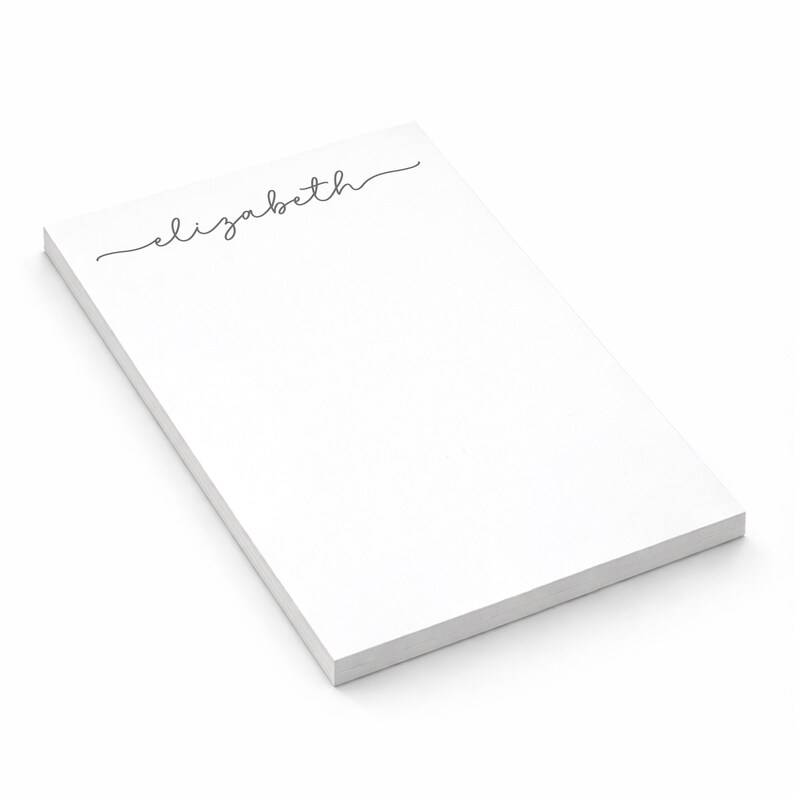 Puede incluir: Un bloc de notas rectangular de color blanco con el nombre elizabeth impreso en una fuente cursiva negra en la parte superior. El bloc consta de una pila de hojas de papel con una superficie limpia y lisa bajo el texto, en &aacute;ngulo.