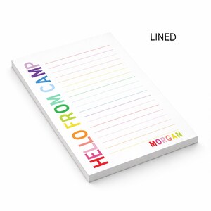 May include: A white rectangular notepad with horizontal lines. The text HELLO FROM CAMP is printed vertically in rainbow colors on the left side. The name MORGAN is printed in rainbow colors at the bottom right. The word LINED appears at the top right.