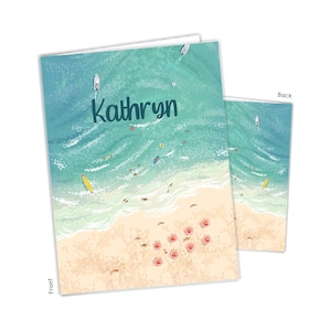 May include: A personalized card with a beach scene featuring turquoise water, white sand, and red umbrellas. The card says "Kathryn" in a blue font.