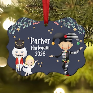 May include: A dark blue scalloped Christmas ornament hanging from a red ribbon. The design features a nutcracker, a ballerina, and a harlequin character with the text Parker Harlequin 2026, surrounded by small gold stars and green holly branches.