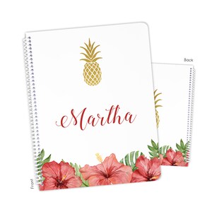May include: A white spiral notebook with a gold pineapple design and the name "Martha" written in red cursive. The bottom of the notebook features a border of red hibiscus flowers and green leaves. The back of the notebook has a gold pineapple design.