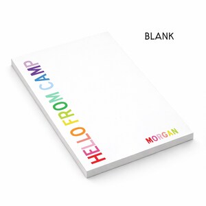 May include: A white rectangular notepad featuring the text HELLO FROM CAMP printed vertically in a rainbow gradient along the left side and the name MORGAN printed in rainbow colors in the bottom right corner, with the word BLANK at the top right.