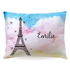 May include: A light blue and pink watercolor pillow with a black outline of the Eiffel Tower and the name "Emilie" written in cursive.