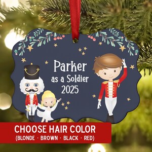 May include: Navy blue Christmas ornament with a red ribbon. The ornament features a cartoon soldier, a nutcracker, and a ballerina. Text reads "Parker as a Soldier 2025" and "Choose Hair Color". The ornament is decorated with stars and greenery.