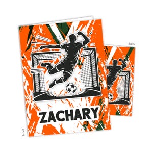 May include: Soccer-themed greeting card with a dynamic illustration of a player kicking a soccer ball towards a goal. The card features the name "ZACHARY" in bold letters against a vibrant orange and green abstract background. The back of the card shows a silhouette of a soccer player.