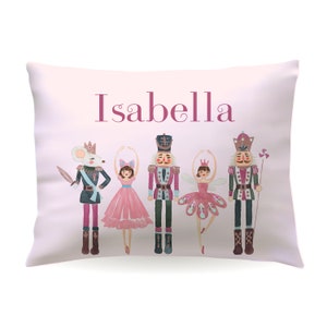 May include: A pink pillow with the name "Isabella" printed in pink letters. The pillow features a watercolor illustration of a mouse, two ballerinas, and two nutcracker soldiers.