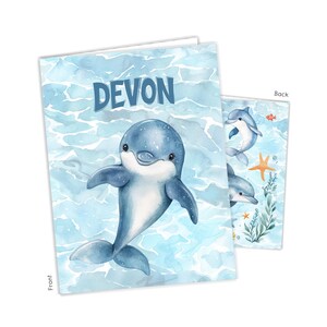 May include: A blue and white watercolor-style card featuring a smiling dolphin with the name "Devon" in blue letters. The background shows a watery scene. The back of the card has additional dolphin illustrations, a starfish, and aquatic plants.