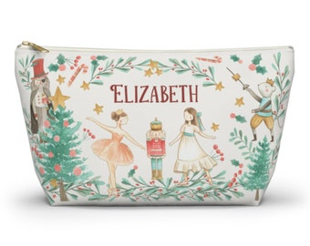 May include: A white zippered pouch with a Christmas Nutcracker theme. The pouch features a ballerina, a nutcracker, a mouse king, and a Christmas tree. The text "ELIZABETH" is printed on the pouch.