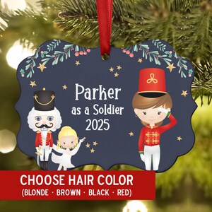 May include: Navy blue Christmas ornament with a red ribbon. The ornament features illustrations of a nutcracker, a ballerina, and a soldier. Text reads "Parker as a Soldier 2025" and "CHOOSE HAIR COLOR (BLONDE BROWN BLACK RED)".