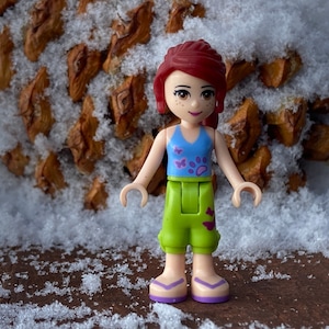Genuine LEGO® Friends minifigure of Mia in lime cropped trousers and a medium blue top with butterfly designs.