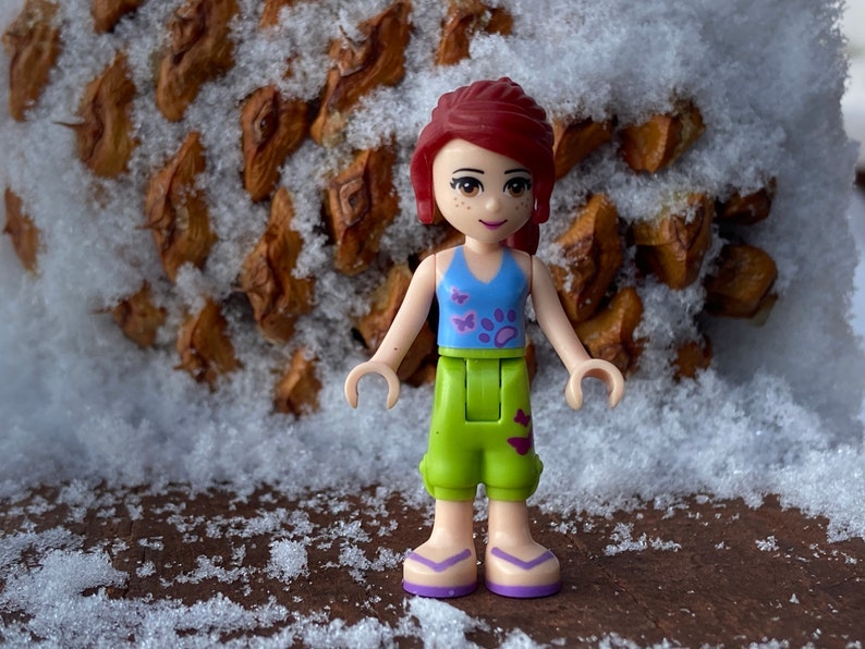 Genuine LEGO® Friends minifigure of Mia in lime cropped trousers and a medium blue top with butterfly designs.
