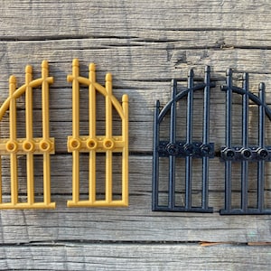 May include: Two sets of decorative gates, one in gold and one in black. Each set is made of plastic and has a curved top with vertical bars. The gates are separated and ready to be assembled.