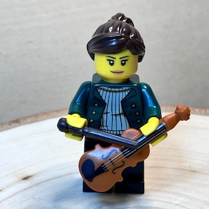 May include: A Lego minifigure of a person with brown hair wearing a green jacket and holding a brown violin.