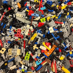 May include: A close-up shot of a pile of colorful plastic building blocks. The blocks are in various shapes and sizes, including bricks, plates, and specialized pieces. Colors include red, blue, yellow, green, gray, and black. The blocks are scattered and overlapping.