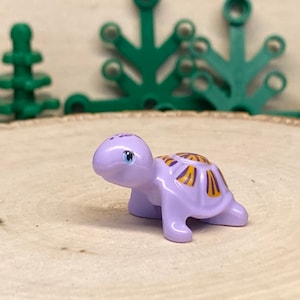 May include: A small purple turtle toy with a yellow and purple shell. The turtle has a friendly face with blue eyes.