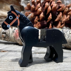 May include: A black toy horse with a brown bridle. The horse is made of plastic and has a simple, blocky design. The horse is standing on a wooden surface.