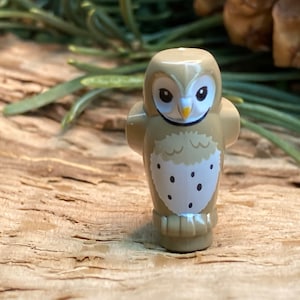 Puede incluir: Una figurita de búho marrón y blanco con un pico amarillo y ojos negros. El búho está de pie sobre una superficie de madera.