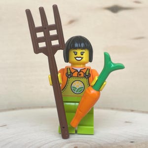 Lady Farmer in Lime Overalls over Orange Shirt, Lime Legs, Black Short Hair holding a Carrot and Pitchfork - Genuine LEGO® Minifigure