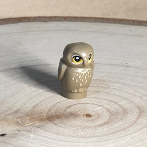 May include: A small brown owl figurine with yellow eyes and white markings. The owl is made of plastic and has a detailed design.