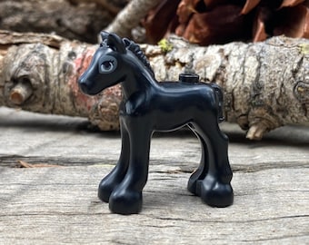 May include: A black toy horse figurine with a detailed mane and tail. The toy horse has a small, round body and four sturdy legs. The horse is standing on a wooden surface.