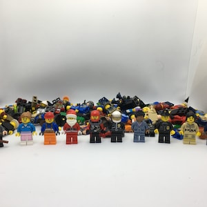May include: A collection of colorful Lego minifigures, including a police officer, a construction worker, a Santa Claus, and a wizard. The minifigures are arranged in a row on a white surface.