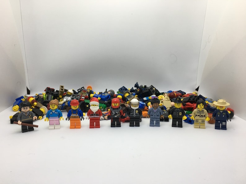 May include: A collection of colorful Lego minifigures, including a police officer, a construction worker, a Santa Claus, and a wizard. The minifigures are arranged in a row on a white surface.