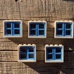 May include: Five white plastic toy windows with blue frames. Each window has two panes of glass. The windows are arranged in a row on a wooden surface.