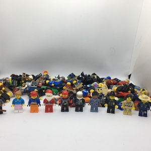 May include: A collection of colorful Lego minifigures, including a police officer, a construction worker, a chef, and a variety of other characters. The minifigures are arranged in a pile on a white surface.