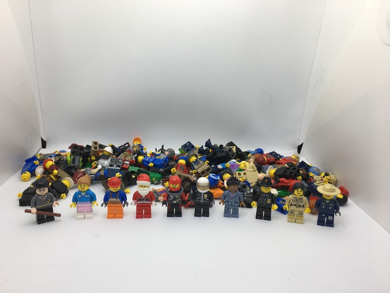 May include: A collection of colorful Lego minifigures, including a police officer, a construction worker, a chef, and a variety of other characters. The minifigures are arranged in a pile on a white surface.