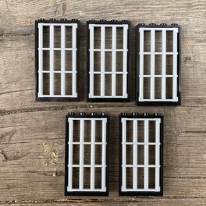 May include: Five black plastic window frames with white bars. The frames are arranged in two rows, with three in the top row and two in the bottom row.