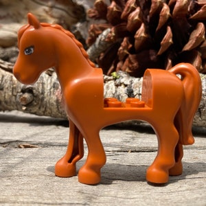 May include: A brown plastic toy horse with a saddle and a tail. The horse has a white eye and is standing on a wooden surface.