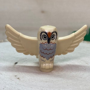 May include: A white owl figurine with outstretched wings. The owl has brown eyes, a black beak, and gray and brown feathers.