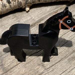 Op de afbeelding: Een zwart speelgoedpaard met een bruine teugel en witte accenten. Het plastic paard heeft een gedetailleerd ontwerp, inclusief een vloeiende staart. Het speelgoed is ontworpen om compatibel te zijn met andere bouwstenen.