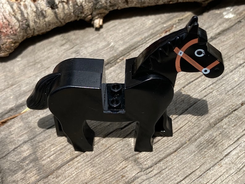 Op de afbeelding: Een zwart speelgoedpaard met een bruine teugel en witte accenten. Het plastic paard heeft een gedetailleerd ontwerp, inclusief een vloeiende staart. Het speelgoed is ontworpen om compatibel te zijn met andere bouwstenen.