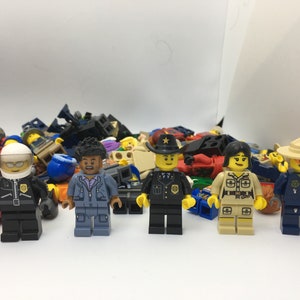 May include: A collection of colorful Lego minifigures, including a police officer, a park ranger, a construction worker, and a pilot. The minifigures are all standing on a white surface.