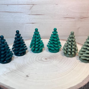 Puede incluir: Seis árboles de pino de plástico en miniatura en varios tonos de verde. Los árboles están dispuestos en una fila sobre una superficie de madera.