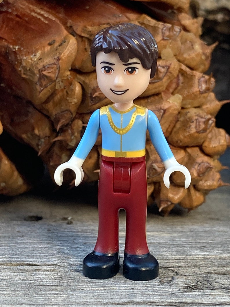 May include: A small plastic figurine of a boy wearing a blue shirt with a gold chain, red pants, and black shoes.