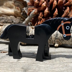 Op de afbeelding: Een zwart plastic paardenspeelgoed met een bruine teugel. Het paard heeft een gedetailleerde manen en staart. Het speelgoed is ontworpen om compatibel te zijn met andere bouwstenen. Het paard staat op een houten oppervlak.