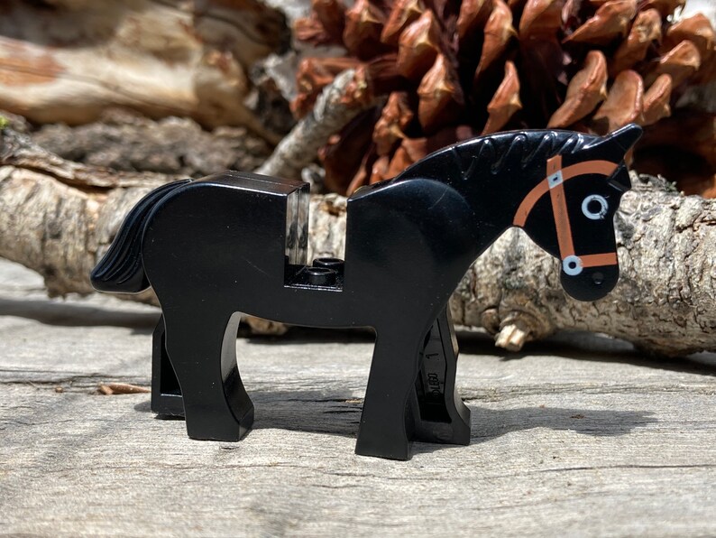 Op de afbeelding: Een zwart plastic paardenspeelgoed met een bruine teugel. Het paard heeft een gedetailleerde manen en staart. Het speelgoed is ontworpen om compatibel te zijn met andere bouwstenen. Het paard staat op een houten oppervlak.
