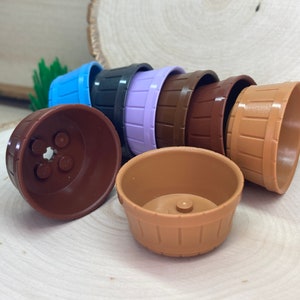 Puede incluir: Un conjunto de ocho macetas pequeñas, redondas, de plástico en varios colores, incluyendo marrón, morado, azul y marrón claro. Las macetas tienen un diseño texturizado de madera.
