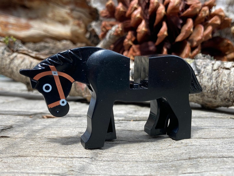 Op de afbeelding: Een zwart plastic speelgoedpaard met een bruine teugel. Het paard heeft een zadelgedeelte en staat op vier poten. Het speelgoed is ontworpen om compatibel te zijn met andere bouwsteensets.